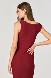 A woman is wearing a sleeveless, form-fitting dress in a deep red color with subtle horizontal stripes. The dress features a wide neckline that drapes off one shoulder.